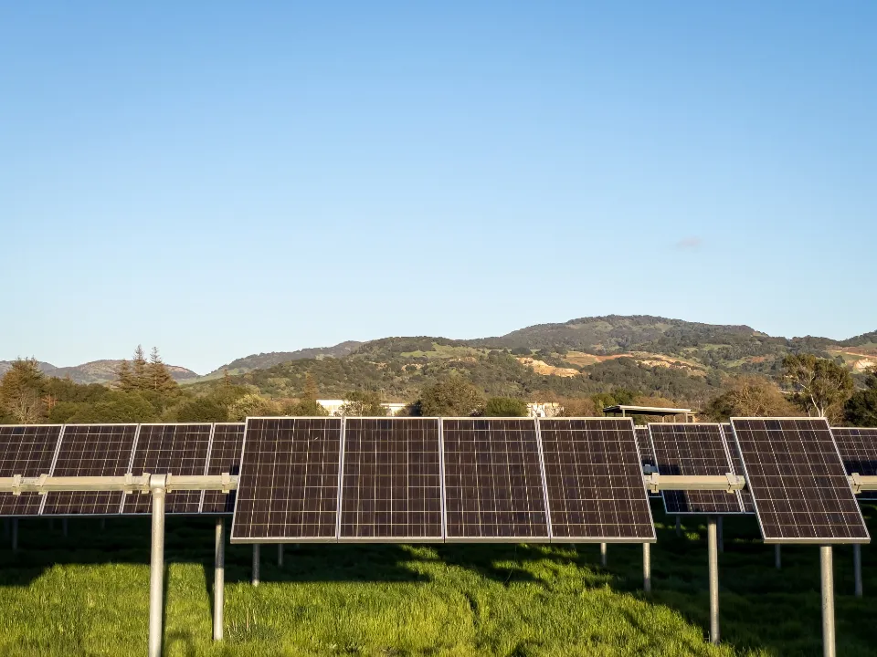 Rows of solar panels on a green field below rolling hills